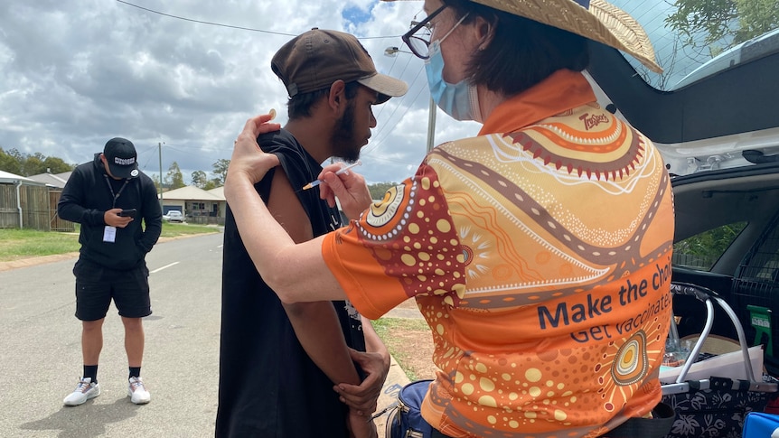 Young Aboriginal man gets vaccinated by health worker on a street in Cherbourg.