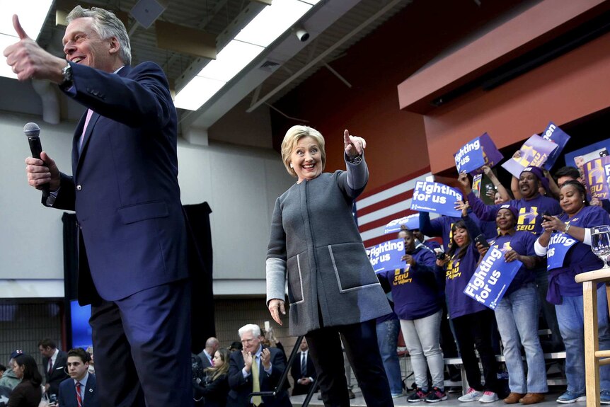 Hillary Clinton points to someone in the crowd as Terry McAuliffe gives the thumbs up, with supporters behind.