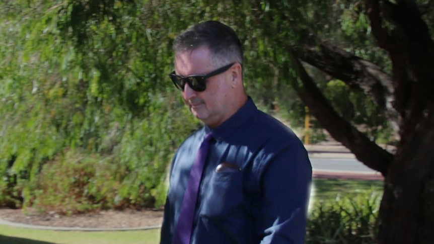 A man wearing a dark shirt and pants walks along a path.