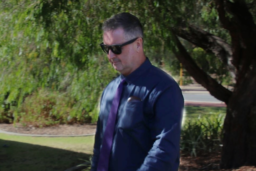 A man wearing a dark shirt and pants walks along a path.