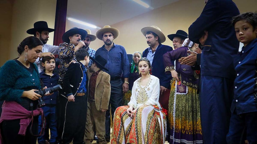 Perty sits on a chair surrounded by men as the marriage ceremony begins to take place.