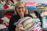 Knit One Give One founder Ros Rogers holds a pile of knitted blankets in various colours at the sorting centre in Caulfield.