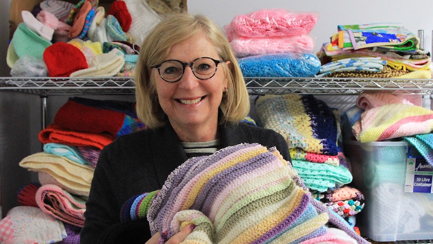 Knit One Give One founder Ros Rogers holds a pile of knitted blankets in various colours at the sorting centre in Caulfield.
