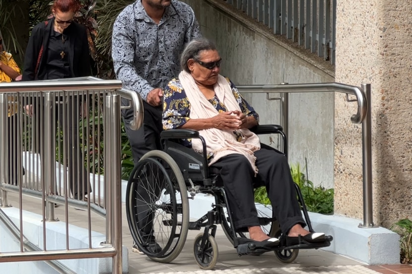 A woman in a wheelchair is wheeled up a ramp by a man in a blue shirt