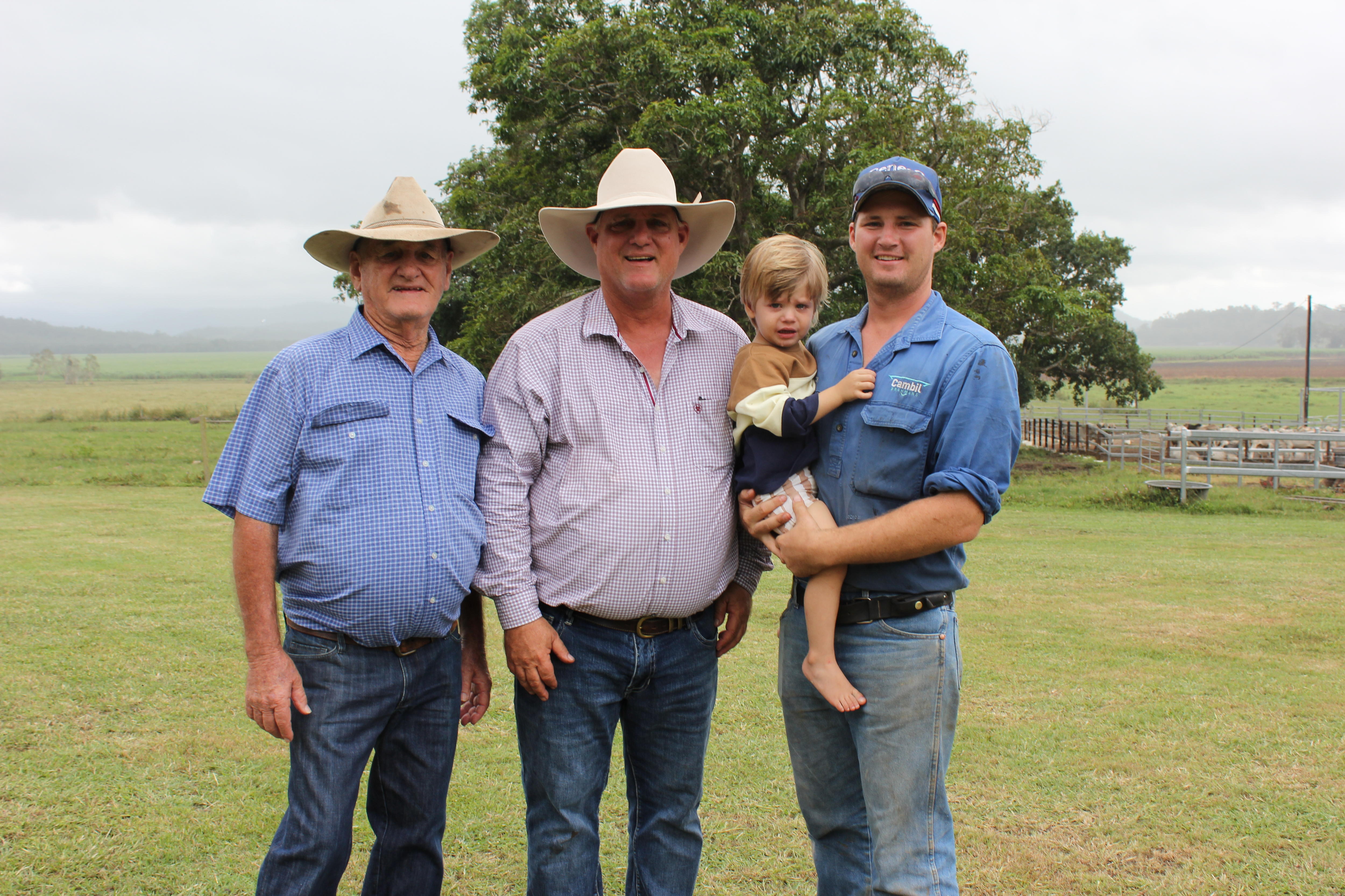Three farmers standing together with the one on the right holding his young son.
