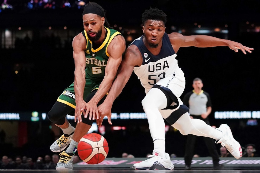 Patty Mills of Australia's Boomers and Donovan Mitchell of USA Basketball reach for a basketball during an exhibition match.