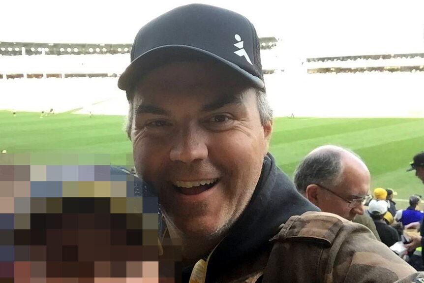 A man takes a selfie at the football next to a person whose face is pixelated