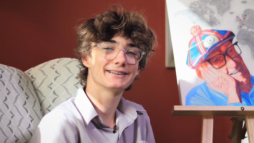 A young boy sits next to a portrait of an old man. 