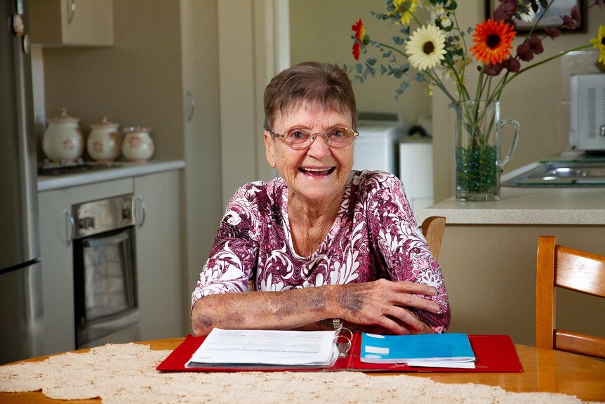 A woman in a purple paisley shirt with a red folder full of bills.