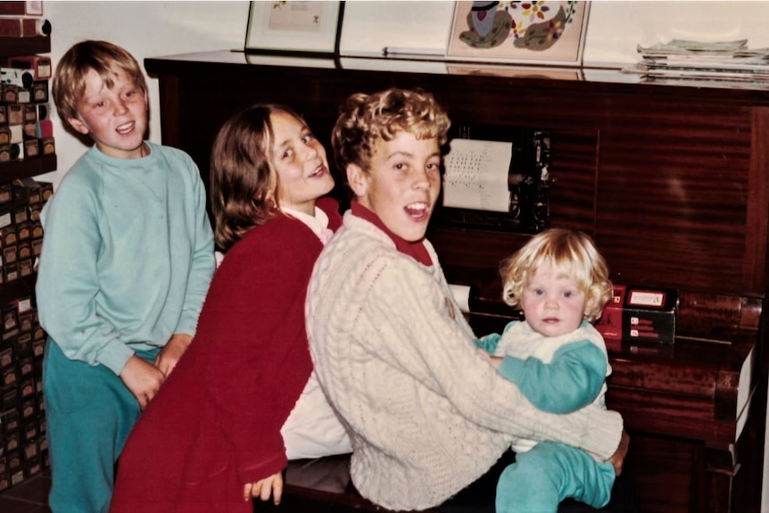 Four young children sit around a piano.