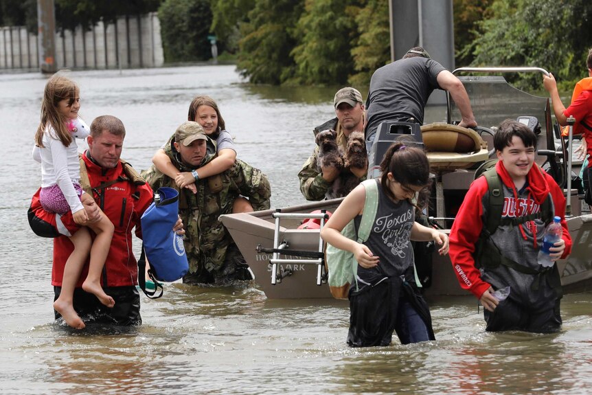 People, carrying possessions and children, walk through murky floodwaters away from a boat