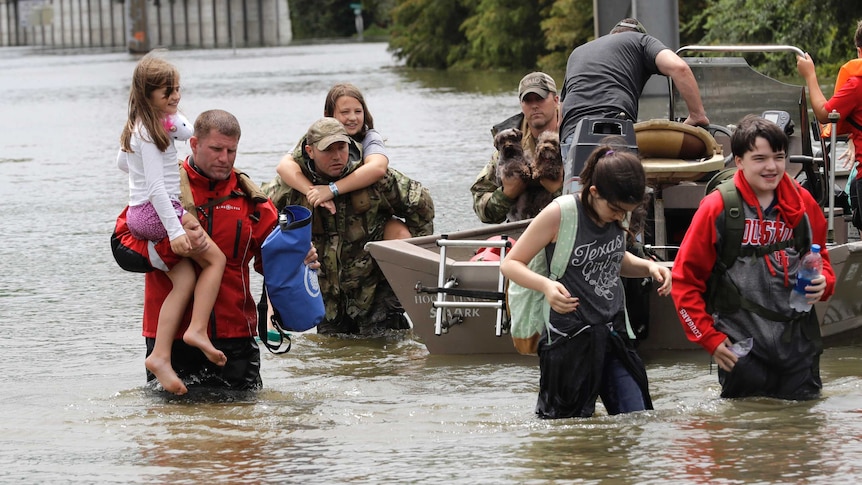 People, carrying possessions and children, walk through murky floodwaters away from a boat