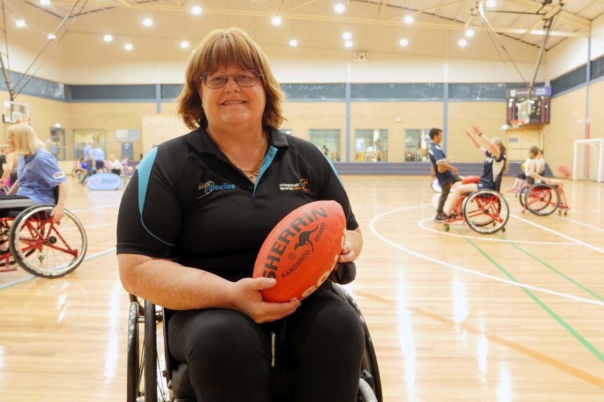 A woman in a wheelchair holds an Aussie Rules football.