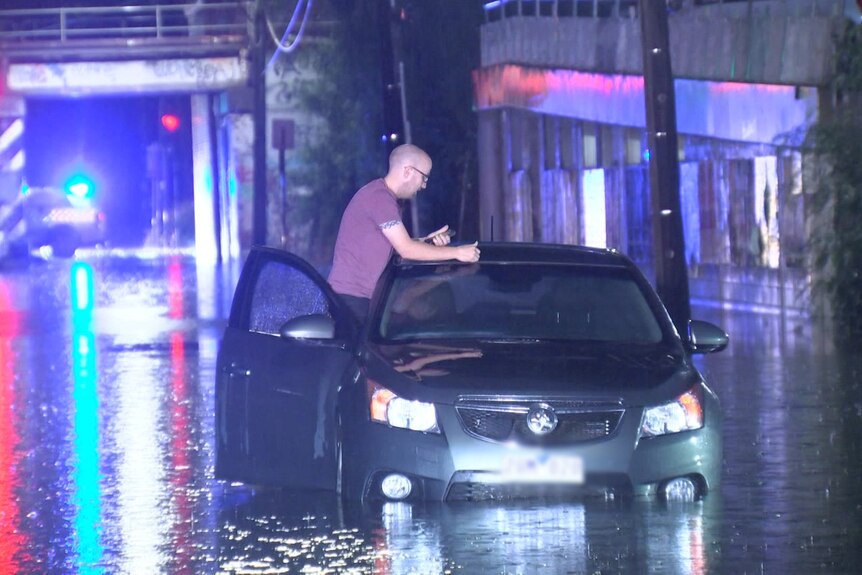 A man standing in his car doorway in floodwater.