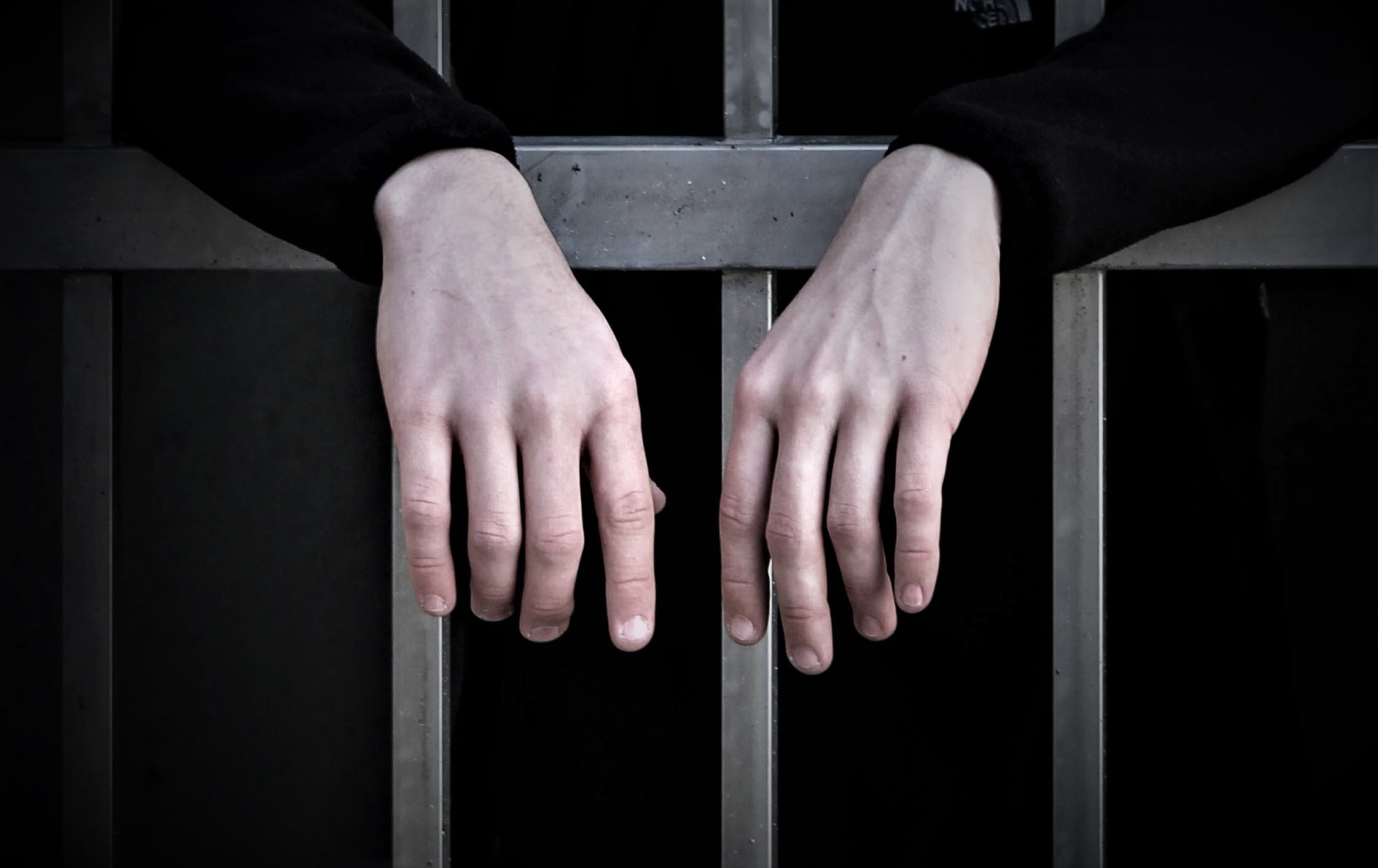 Hands resting on prison cells bars.