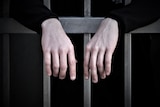 Hands resting on prison cells bars.