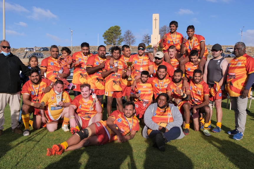 Team photo of Parntu Warriors on the oval with their grand final trophy.