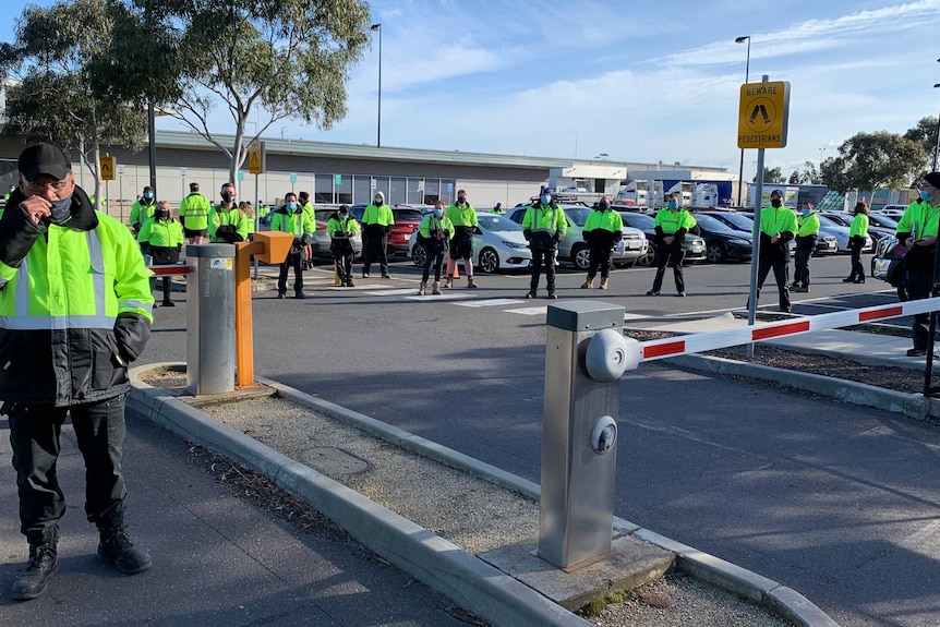 Union members all wearing green fluro stand outside the Woolworths Distribution Centre.