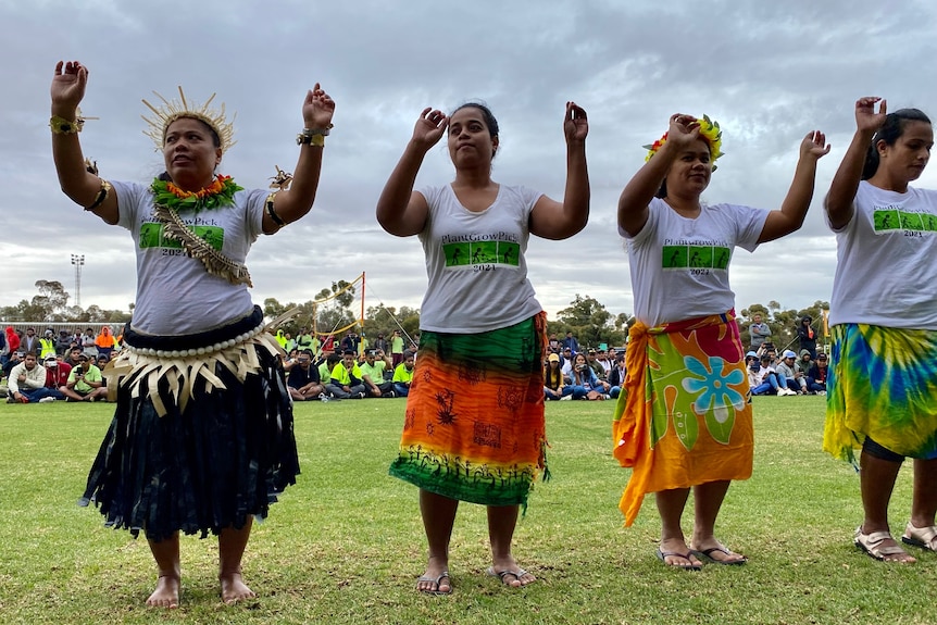 Four women in islander clothes performing a traditional dance, their arms uplifted