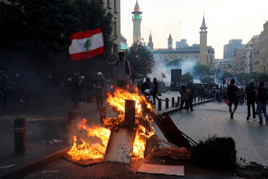 A man holds up a Lebanese flag near a fire as protesters march through the streets near parliament