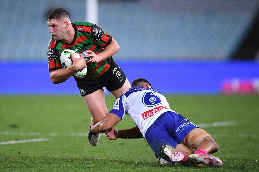 A South Sydney NRL player is tackled around the knees by a Canterbury opponent.