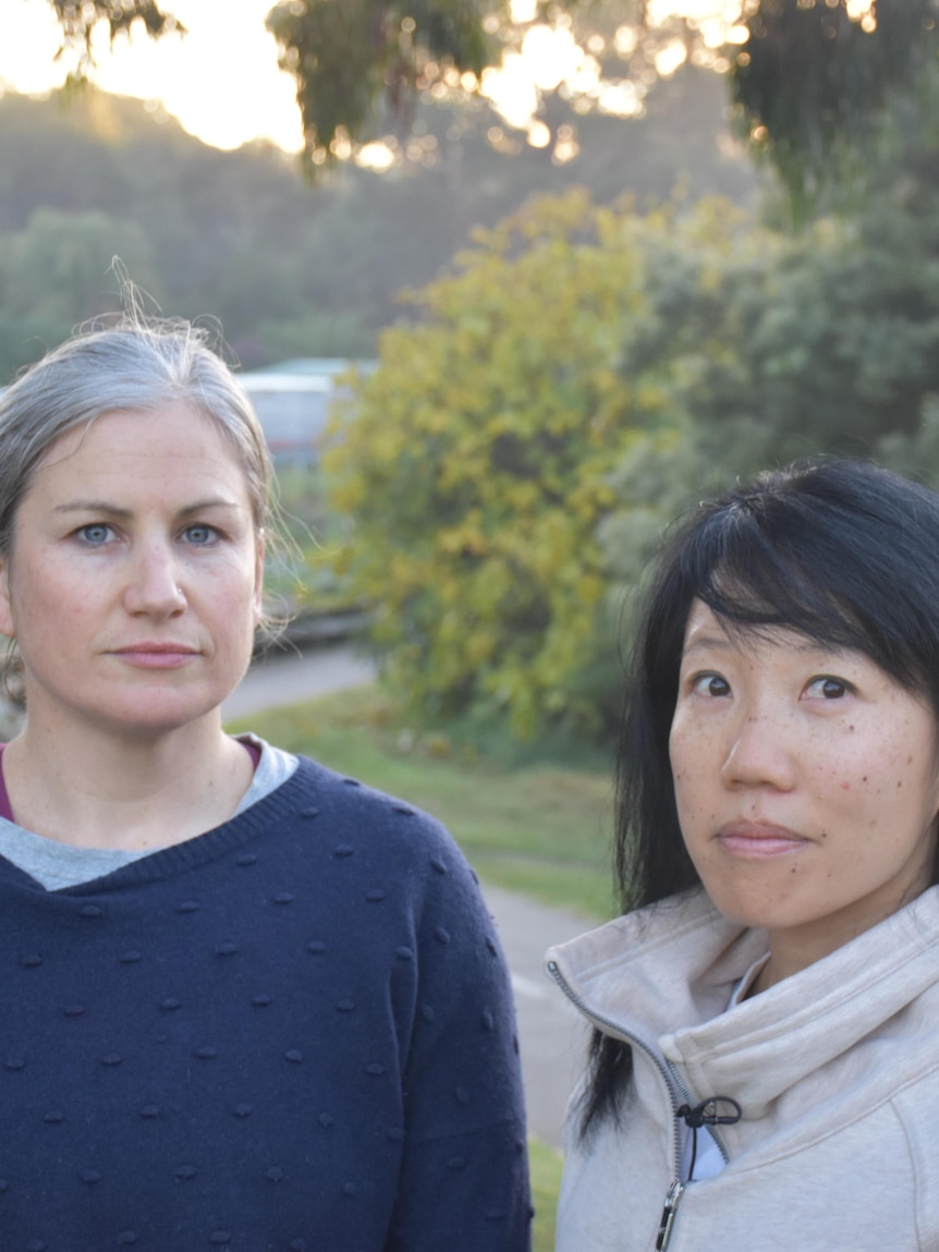 Two women looking at the camera with a cyclist passing in the background.