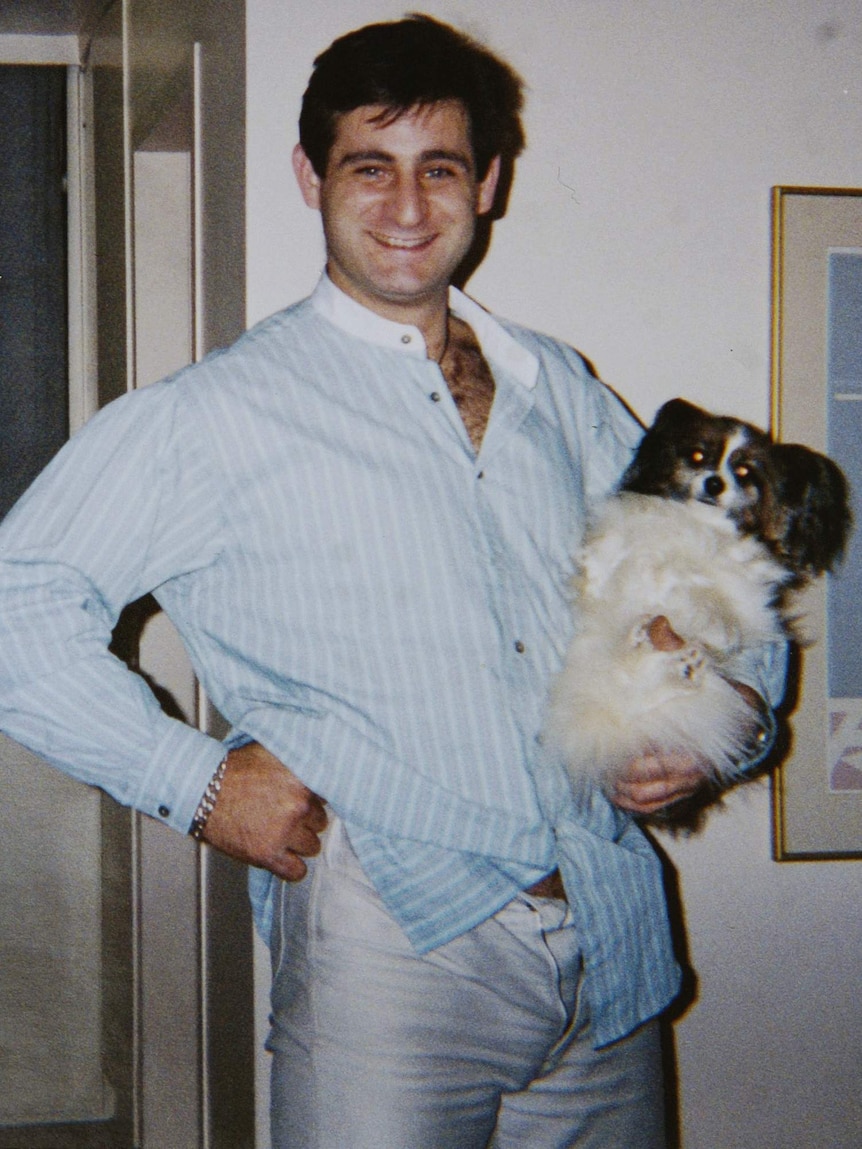 A man wearing a blue and white striped shirt holds a small white dog.