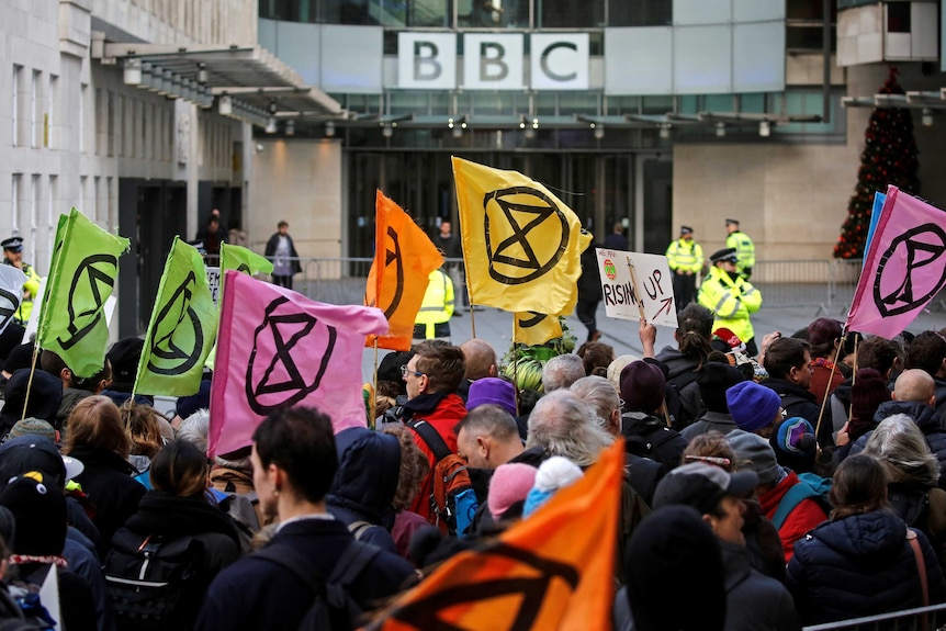 Protesters wave Extinction Rebellion banners outside in front of a building with a BBC sign