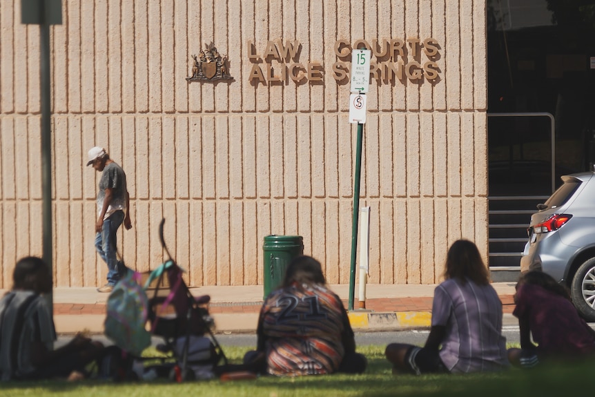 A man walking past the Alice Springs Local Court, with a small group sitting on the grass in the foreground.