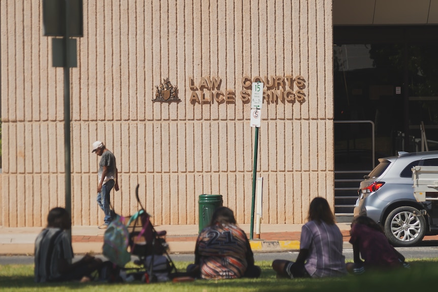 A man walking past the Alice Springs Local Court, with a small group sitting on the grass in the foreground.