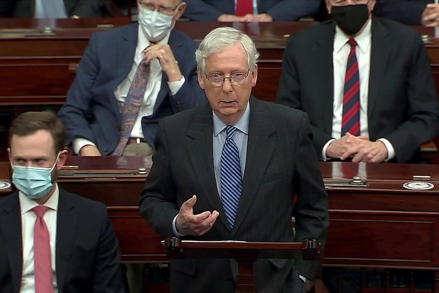 Mitch McConnell stands in the Senate next to people with masks on