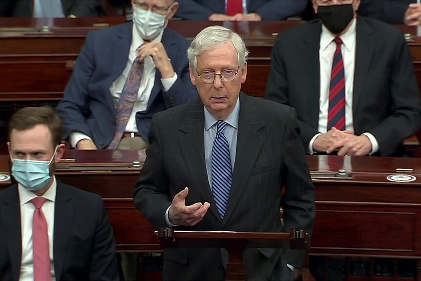 Mitch McConnell stands in the Senate next to people with masks on