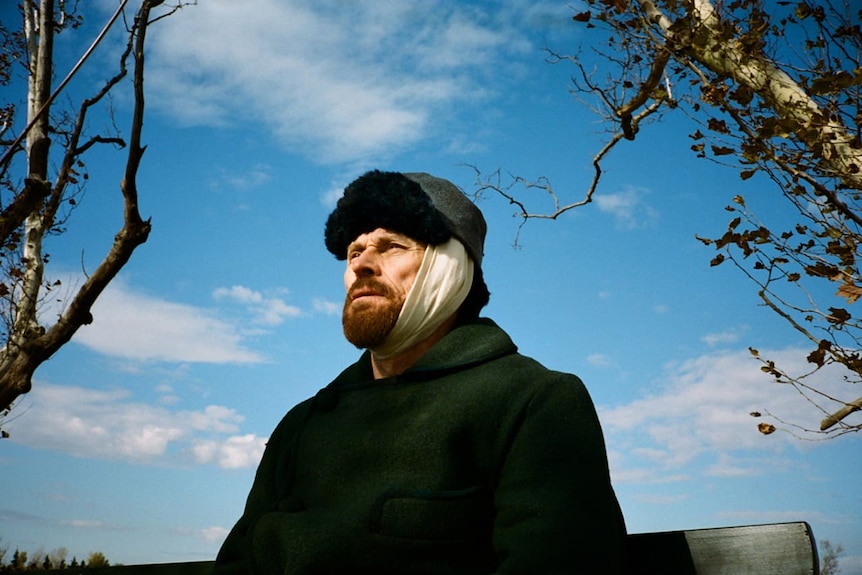 Colour still of Willem Dafoe sitting outdoors looking at sun in 2018 film At Eternity's Gate.