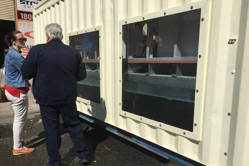 A man and woman stand alongside a cabin with a prototype of an amphibious home