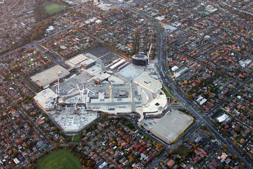 A large complex of buildings, topped by cranes, surrounded by suburbia.