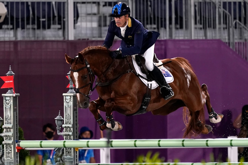 An Australian male competitor in the team equestrian eventing competition rides his horse over a hurdle.