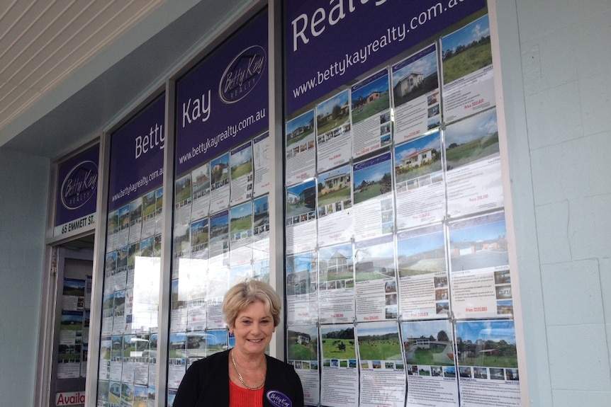 Real estate agent standing in front of shop-front in north-west Tasmania, will photos of properties in the window