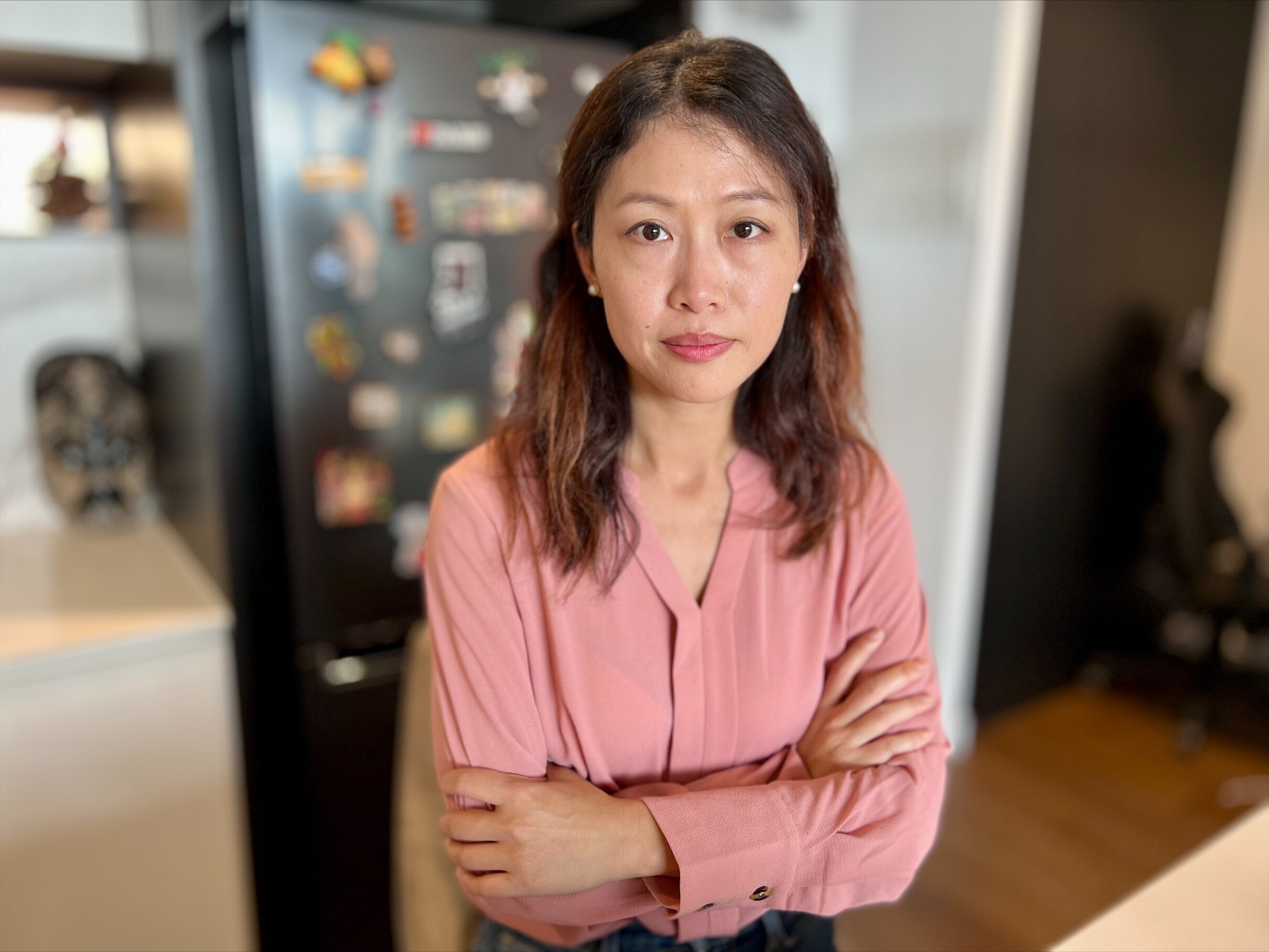 A woman in a pink shirt crosses her arms.