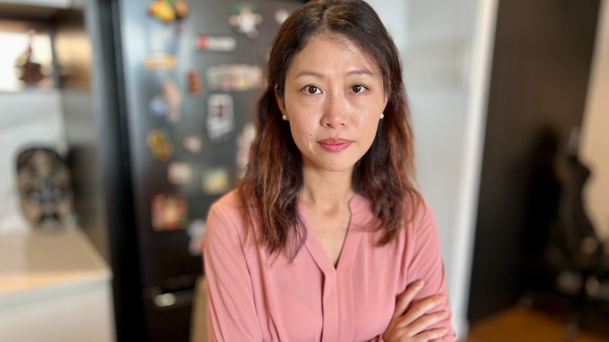 A woman in a pink shirt crosses her arms.