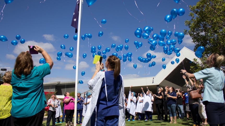 People standing in a circle releasing blue balloons into the sky.