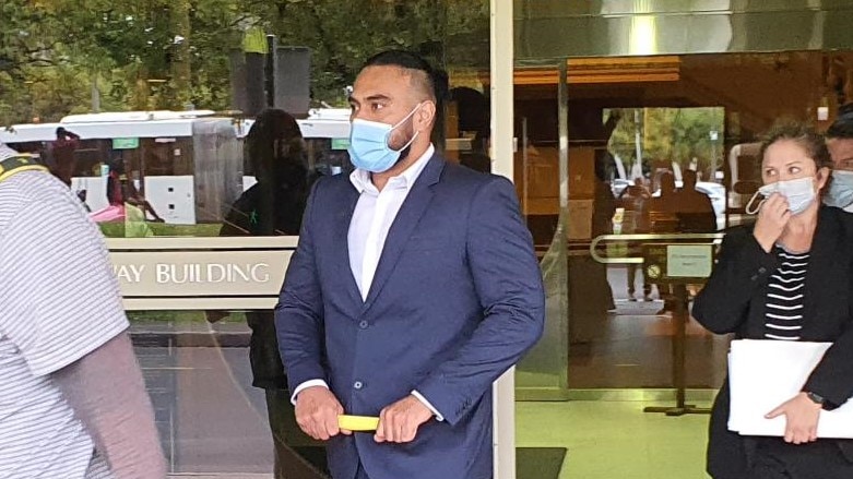 A man in a suit wearing a face mask walks out of a court building