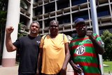 Three people stand in front of a courthouse in Cairns
