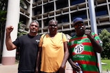 Three people stand in front of a courthouse in Cairns