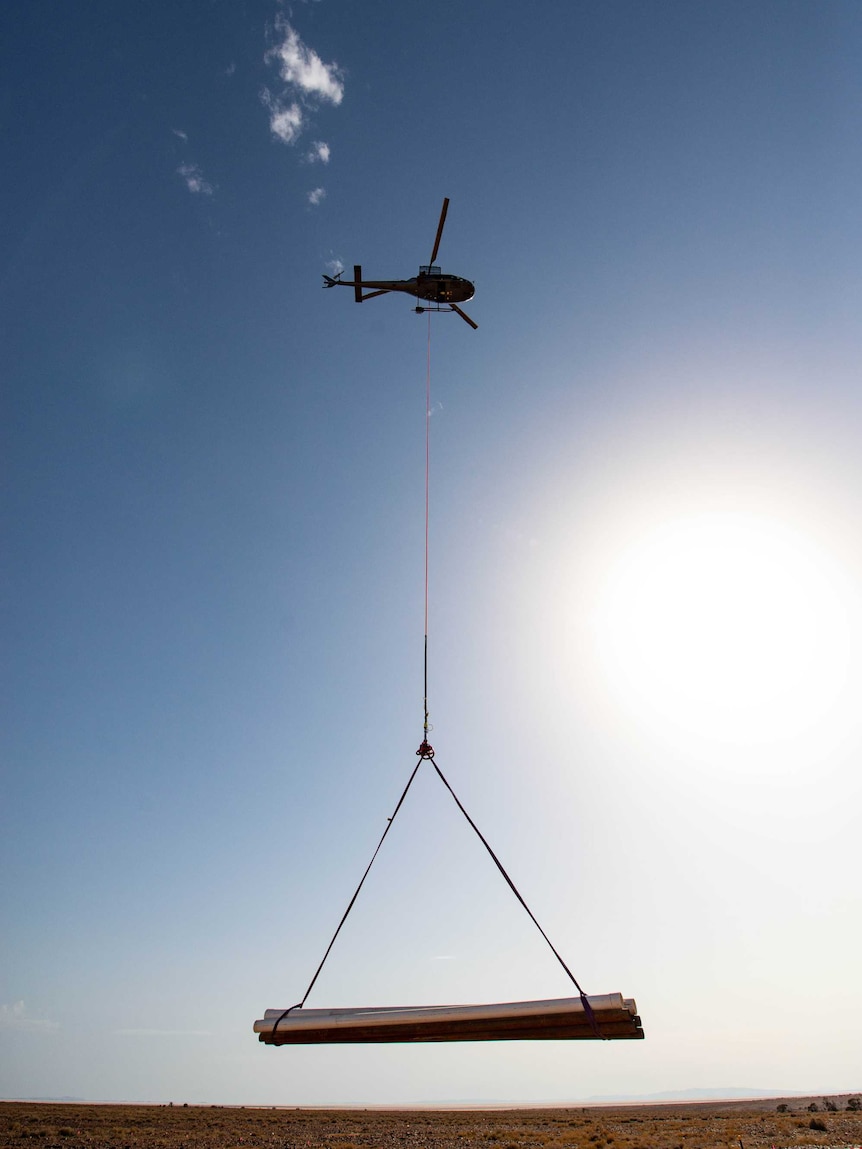 A helicopter carries a large platform over a plain white surface.
