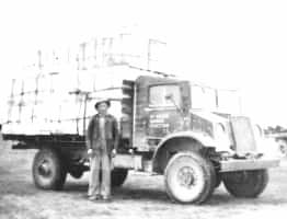 A black and white photograph of a young boy and an old truck loaded with wool bales