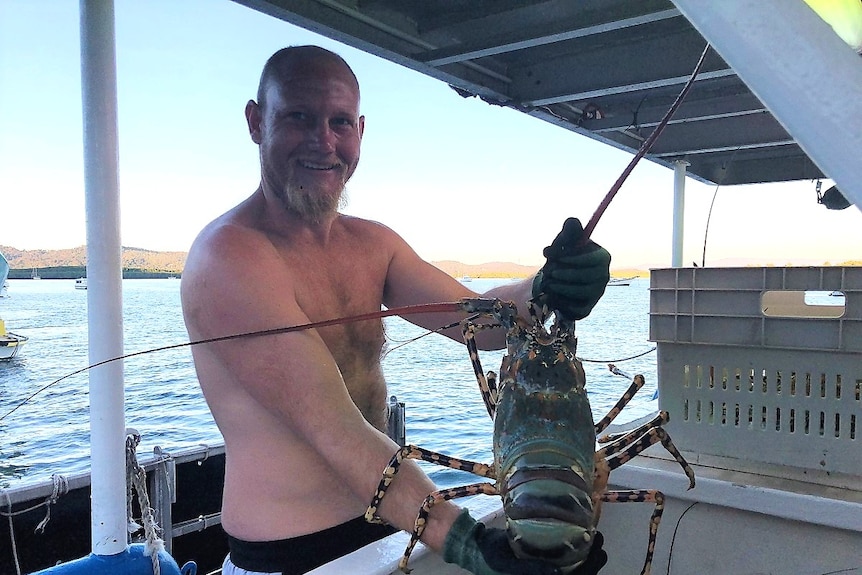 Shirtless man on boat holding large crayfish