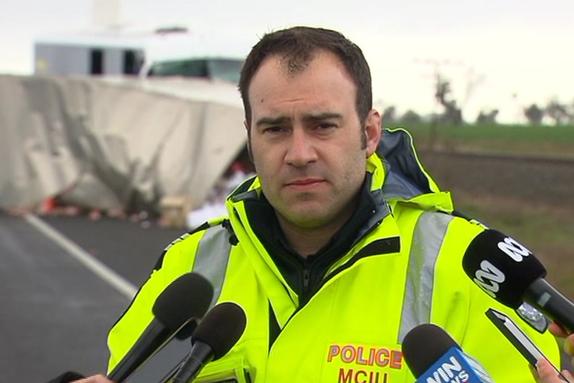 A police officer speaks to media at the site of a bus and truck crash.