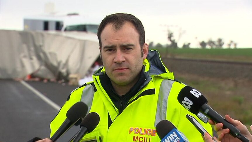 A police officer speaks to media at the site of a bus and truck crash.