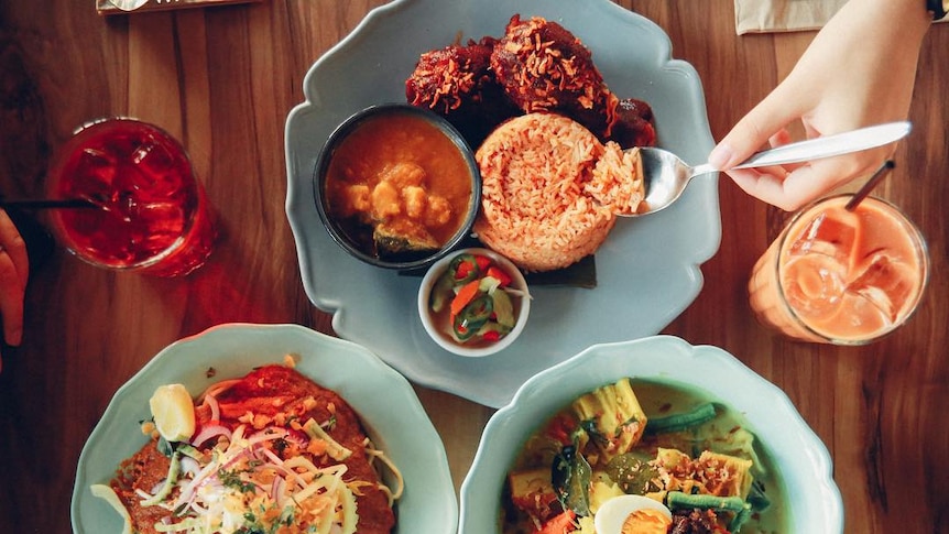 Overhead shot of three plates of Malay food and two drinks.