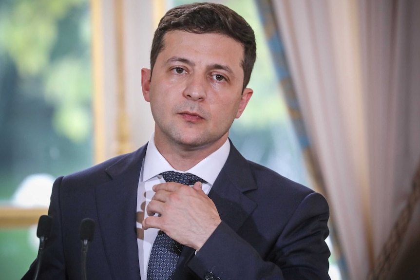 Volodymyr Zelensky stă în fața oglinzii, ajustându-și cravata.